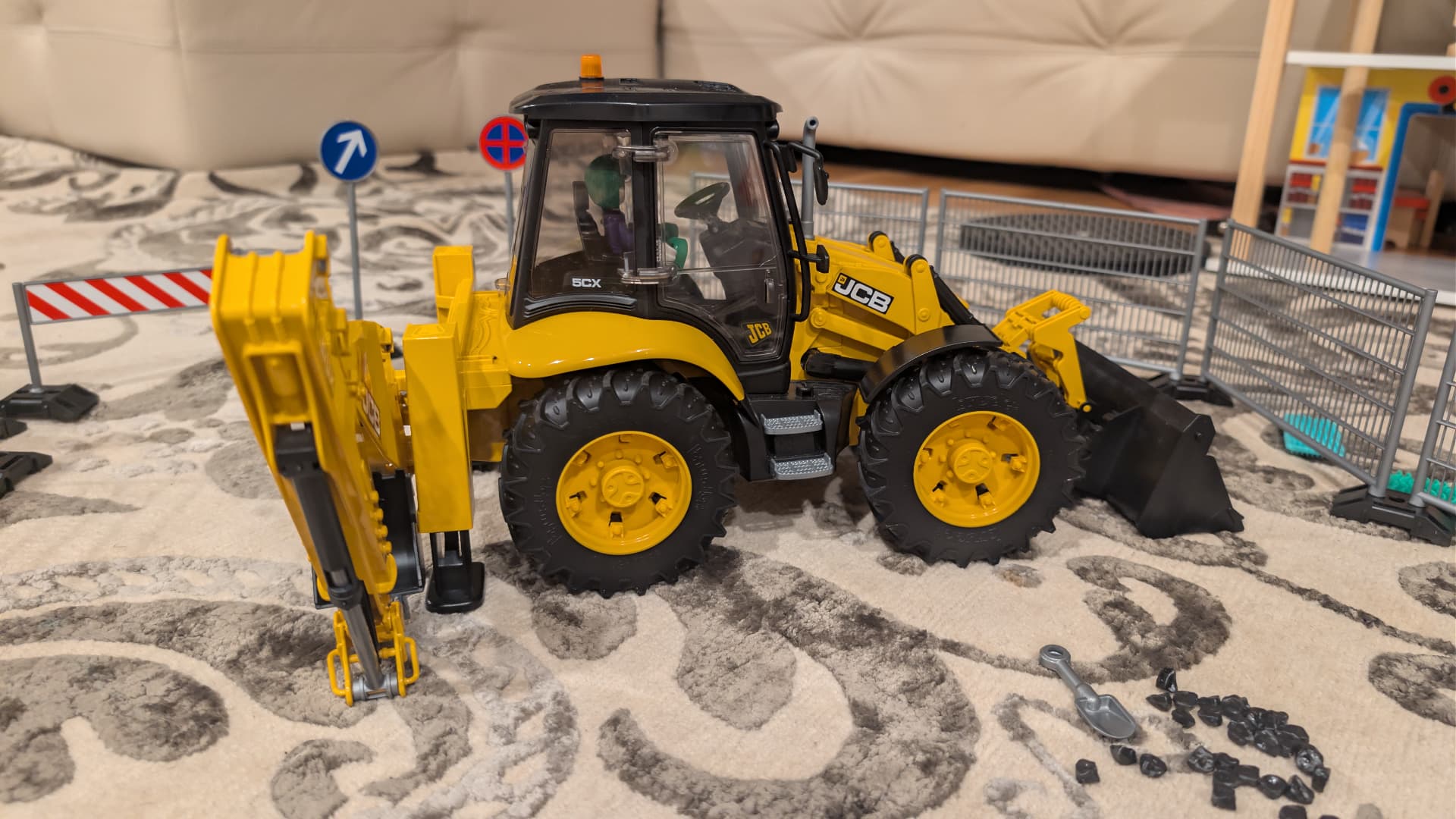 A yellow Bruder JCB backhoe loader on a living room rug with road signs and gravel